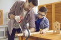 Dad teaches his little interested son to build a wooden toy house in the workshop.