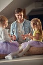 Dad is teaching his little daughters how to drum with spoons on the furniture. Family, home, playing, togetherness Royalty Free Stock Photo