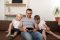 Dad and two sons are sitting on couch and watching video on phone. Family leisure Royalty Free Stock Photo