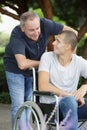 Dad walking with disabled son in wheelchair at park Royalty Free Stock Photo