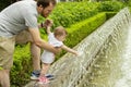 Dad walks with his little daughter in the park with fountains. Baby girl 10 months pulls hands to jets of water in a fountain Royalty Free Stock Photo