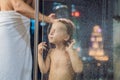 Dad washes his son`s hair in the shower in the evening before going to sleep on the background of a window with a panoramic view