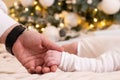 Dad& x27;s hand holds the hand of a newborn baby under the New Year tree, love and care of the family, the hand of a Royalty Free Stock Photo