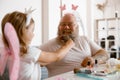 Daddy with headband plays with little daughter in fairy suit at table in light room Royalty Free Stock Photo