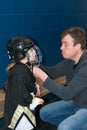 Daddy helps little cute blonde girl to wear hockey helmet. Girl is wearing in full hockey equipment