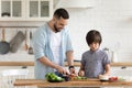 Daddy and little son preparing vegetable salad together in kitchen