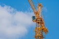 Operator cab on large yellow industrial crane against cloudy sky