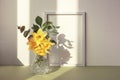 Daffodil bouquet in glass vase and picture frame against white wall in sunlight. Spring concept Royalty Free Stock Photo