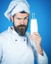 Dairy farmer products. Professional male chef in white apron with glass bottle of milk. Serious bearded cook in chef hat Royalty Free Stock Photo