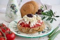 Dakos traditional Greek appetizer on a traditional plate with ceramic olive oil jar, dry rye bread, olives and olive branch.