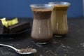 Dalgona coffee and cocoa in glass transparent glasses. Nearby lies a metal spoon with instant coffee, and a chocolate dessert on a