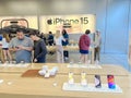Large iPhone 15 wall poster and customer shopping for latest models on wooden table display at Apple Store in downtown, chain of