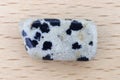 Dalmatian jasper stone texture on light varnished wood background. Macro closeup