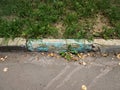 Damadged old curb painted aquamarine needs to be replaced. Yellow leaves on asphalt. Royalty Free Stock Photo