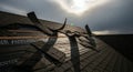 Damaged Black Asphalt Roof with Missing Shingles Under Dramatic Sky Bright Sun Breaking Through Stormy Clouds Royalty Free Stock Photo