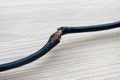 Damaged black electric cord on wooden floor background. Dangerous broken electrical cable Royalty Free Stock Photo