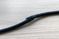 Damaged black electric cord on wooden floor background. Dangerous broken power cable