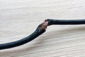 Damaged black electric cord on wooden table or floor background. Dangerous broken electrical cable