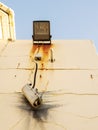 Damaged CCTV camera hanging on a cable on yellow wall, old flood light above the camera. Front element is broken and there is sign Royalty Free Stock Photo