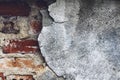 Damaged grey wall with red bricks peeking through.