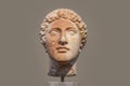 Damaged head of ancient Greek statue with part of face rough and orange from deterioration isolated against tan background