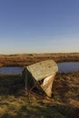 A damaged old Wooden Fishing Boat with its Rusting metal Anchor laying on the Grass banks