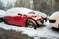 Damaged red car, with a bent hood, covered with snow, sitting in an auto service yard