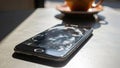 Damaged smartphone, shattered screen on table, coffee blurred, repair needed Royalty Free Stock Photo
