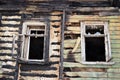 The damaged wall of the house from the fire and two windows with broken glass in the rays of the setting sun in the spring Royalty Free Stock Photo