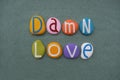Damn love, negative message composed with multi colored stone letters over green sand