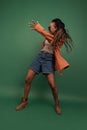 Emotional african girl in shorts and shirt dancing, having fun isolated on dark green background. Concept of beauty, art Royalty Free Stock Photo