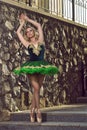 Dance Photography. Portrait of Dancing Professional Caucasian Ballerina in Green Tutu Dress Posing Against Stony Wall Ourdoors