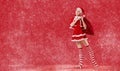 Dancing ballerina girl in pointe shoes with a gift in her hands dressed as Santa Claus on a red background