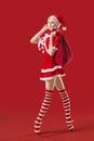 Dancing ballerina girl in pointe shoes with a gift in her hands dressed as Santa Claus on a red background