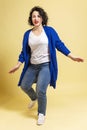 Dancing beautiful young woman plus size in jeans and a blue jacket. Yellow background. Vertical Royalty Free Stock Photo