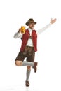 Dancing, celebrating. Young emotional mustache man in hat, wearing folk Bavarian or german clothes, holding beer mug Royalty Free Stock Photo