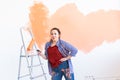 Dancing funny female painting the wall with paint roller. Portrait of a young beautiful woman painting wall in her new Royalty Free Stock Photo