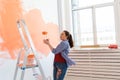 Dancing funny painting the wall with paint roller. Portrait of a young beautiful woman painting wall in her new Royalty Free Stock Photo