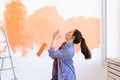 Dancing funny young woman painting interior wall with paint roller in new house. A woman with roller applying paint on a Royalty Free Stock Photo