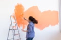 Dancing funny young woman painting interior wall with paint roller in new house. A woman with roller applying paint on a Royalty Free Stock Photo