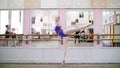 in dancing hall, Young ballerina in purple leotard performs developpe attitude on pointe shoes, raises her leg up behind