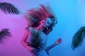 Dancing in neon. A girl with long blonde hair is dancing at a beach party. Summer dance to the music on the background of tropical Royalty Free Stock Photo