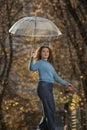 Dancing young woman with long hair walks through autumn park. Pretty girl with transparent umbrella