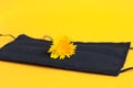 A dandelion flower lies on a black protective mask on a yellow background, close-up-the concept of the impossibility of a