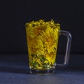 Dandelion yellow flower tea drink in glass, closeup. Concept of healthy eating. Herbal tea in glass cup and flowers on black Royalty Free Stock Photo