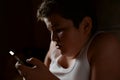 Danger addiction internet concept of thick little boy in white tank top playing cellphone in darkness