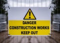 Danger construction site keep out modern clean yellow sign with triangle exclamation mark attached to metal compound fence around Royalty Free Stock Photo