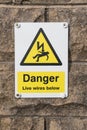 Danger Live Wires Below Warning Sign on a stone brick wall