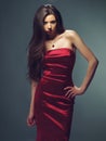 Danger never looked so tempting. Fashion model posing sensually in a fitting red satin dress against a dark background. Royalty Free Stock Photo