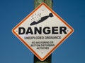 Danger unexploded ordnance on a post with brilliant blue sky